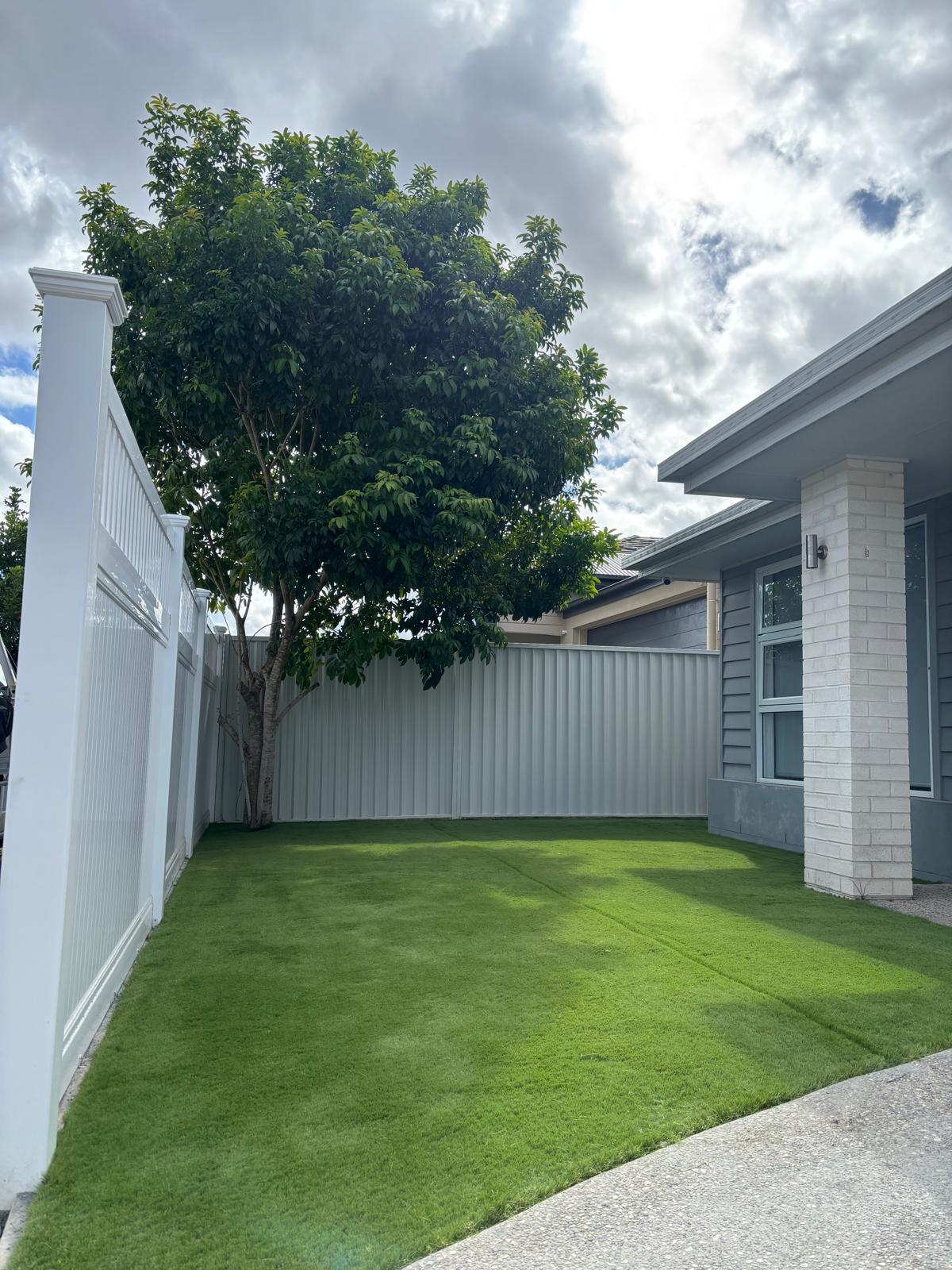 Newly laid synthetic grass beside house and fencing.